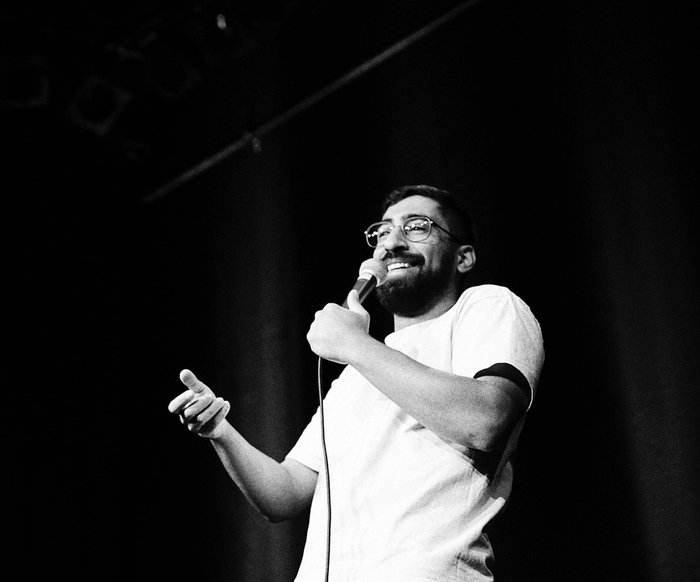 Ein schwarz-weiß Foto von Kawus Kalantar wie er ein Mikrofon in der Hand hält und auf einer Bühne steht.