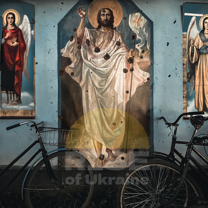 Zwei Fahrräder stehen vor einer Heiligenabbildung. Das Gemälde ist mit Einschusslöchern übersäht.