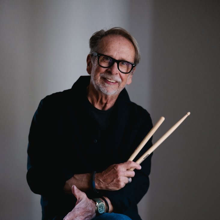 Ein Mann sitzt auf einer großen Trommel mit Drumsticks in der Hand