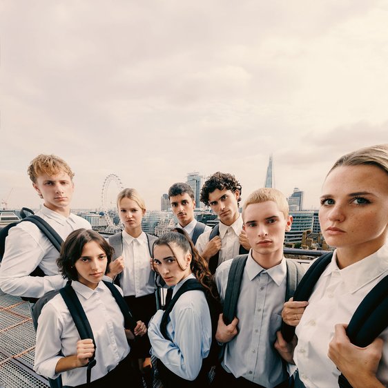 Die Tänzer:innen der Gauthier Dance JUNIORS stehen eng beieinander in hellen Hemden und Blusen mit Rucksäcken und blicken direkt in die Kamera.