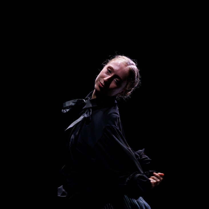 Die Tänzer:innen von Gauthier Dance in schwarzen Kostümen auf der Bühne. Die Bühne ist auch dunkel und es gibt wenig Licht.