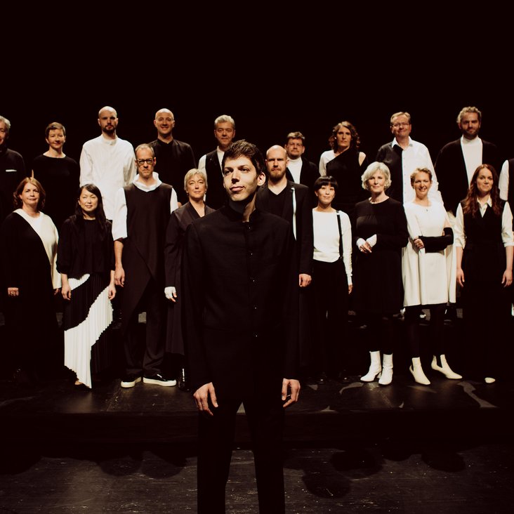 Großes Vokalensemble auf einer Bühne, Gruppenaufstellung unter Bühnenlicht.
