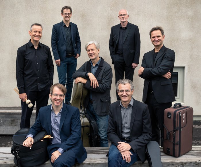 Die Musiker sitzen und stehen beisammen und schauen alle in die Kamera. Ihre Instrumente sind in die jeweiligen Koffer verpackt.
