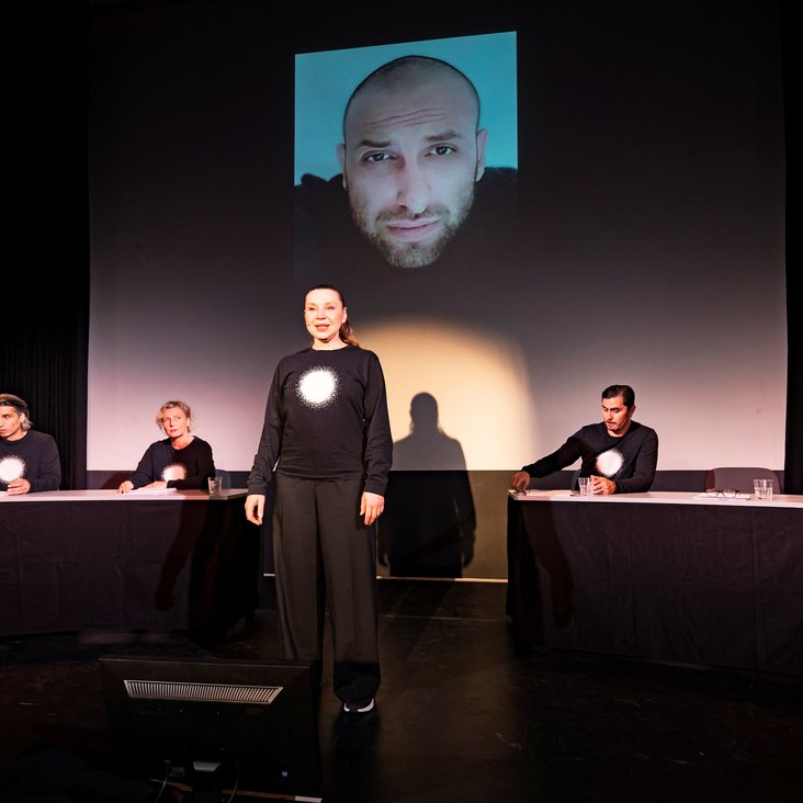 Die Schauspieler:innen von "And now Hanau" auf der Bühne. Sie tragen alle schwarze Kleidung mit einem vollflächig weißen Kreis auf der Brust.