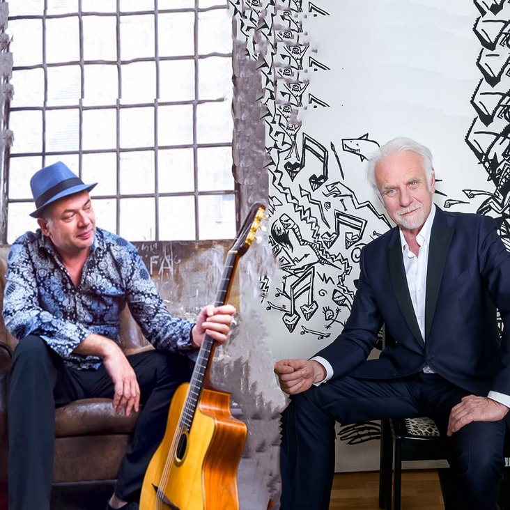 Zwei Musiker sitzen einander gegenüber, getrennt durch eine vertikale Bildkante; zwischen ihnen steht eine Akustikgitarre.
