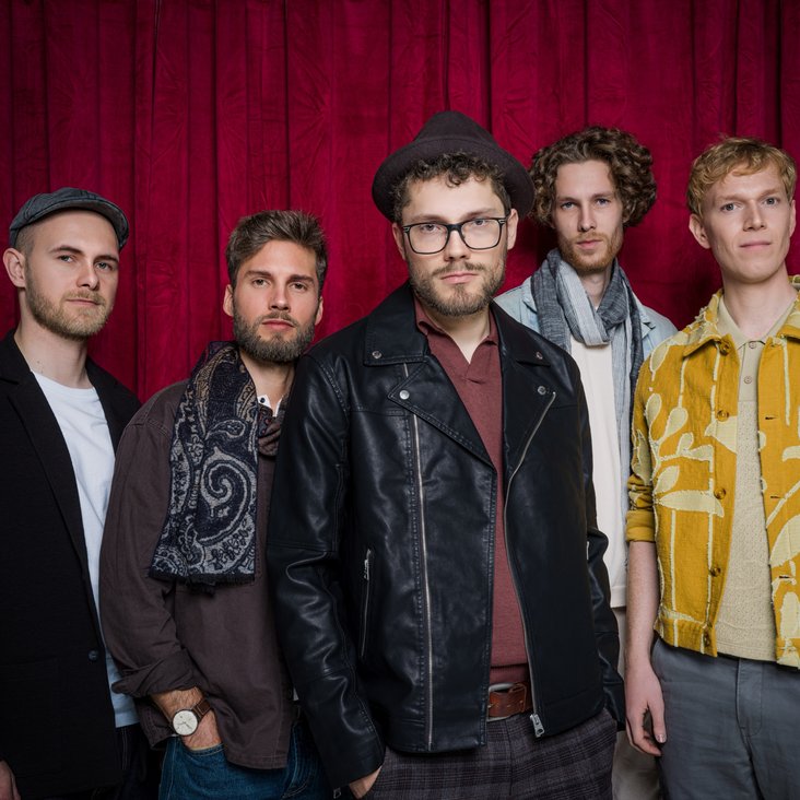 Die fünf Bandmitglieder von "anders" stehen vor einem roten Vorhang und blicken in die Kamera