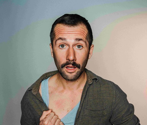 Portraitfoto von Stefan Leonhardsberger. Er schaut mit geöffnetem Mund in die Kamera, er trägt ein grünes Hemd, darunter ist ein blaues Unterhemd zu sehen.