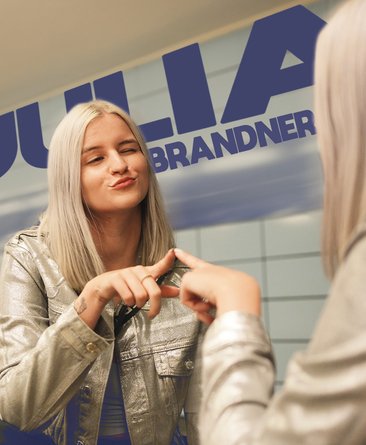 Julia Brandner vor einer Spiegelwand, sie berührt mit der Hand den Spiegel.