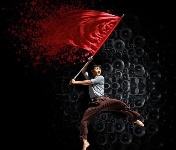 Ein Tänzer schwingt im Sprung eine rote Flagge, welche sich am Ende auflöst. Im Hintergrund sind Lautsprecher.