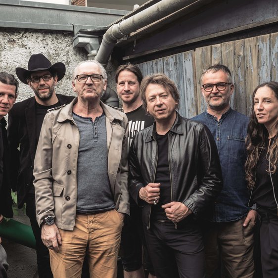 Die Gruppe von Musiker:innen vor einem Gebäude aus Stein und Holz.
