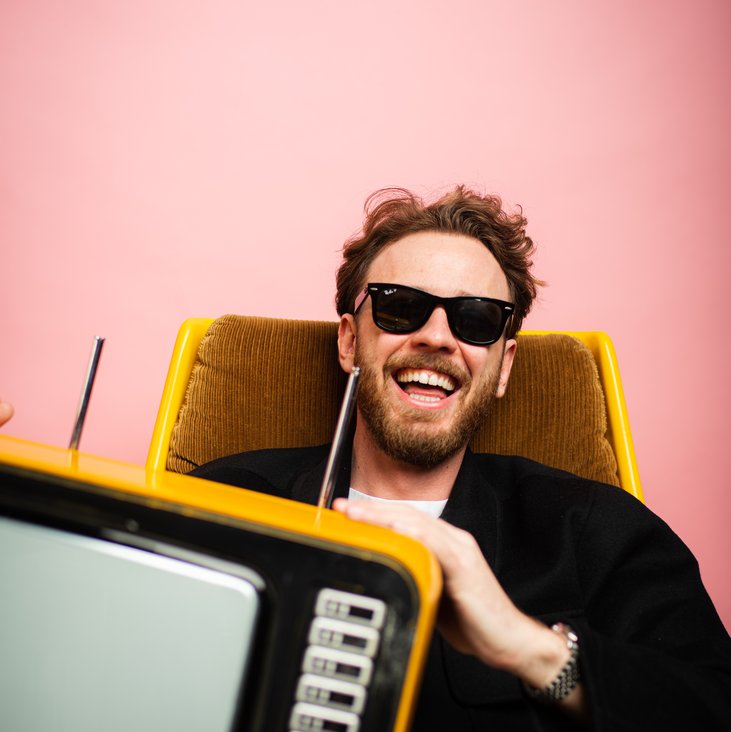Marco Gianni lacht mit einem alten TV Gerät auf dem Schoß