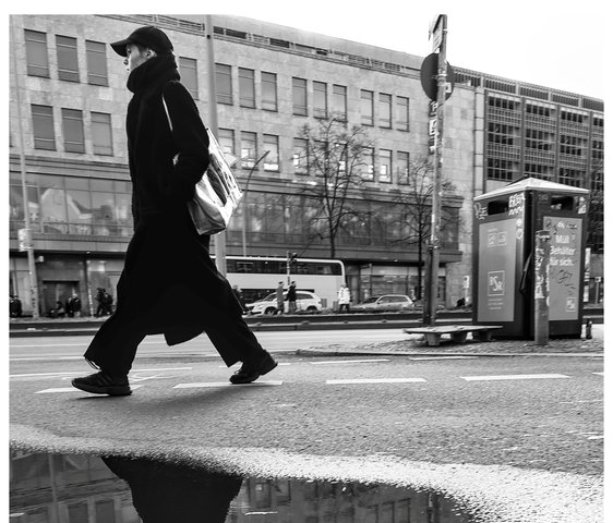 Ein Mensch geht durch eine Straße von Berlin und spiegelt sich dabei in einer Pfütze.