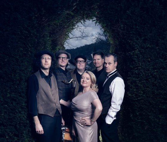 Die Musiker:innen von "Youkali" stehen vor einem pflanzenbewachsenen Torbogen, das Foto hat eine dunkle, aber keine düstere Atmosphäre