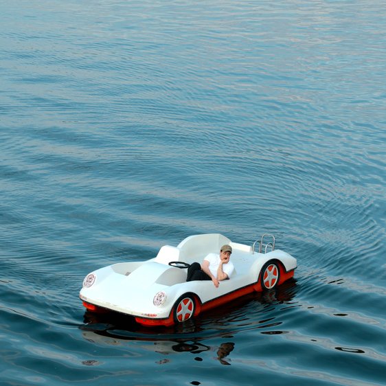 Fred Costea in einem Boot, das die Form eines Autos hat auf einem See oder ähnlichem.