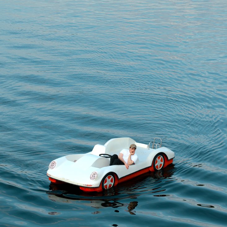 Fred Costea in einem Boot, das die Form eines Autos hat auf einem See oder ähnlichem.