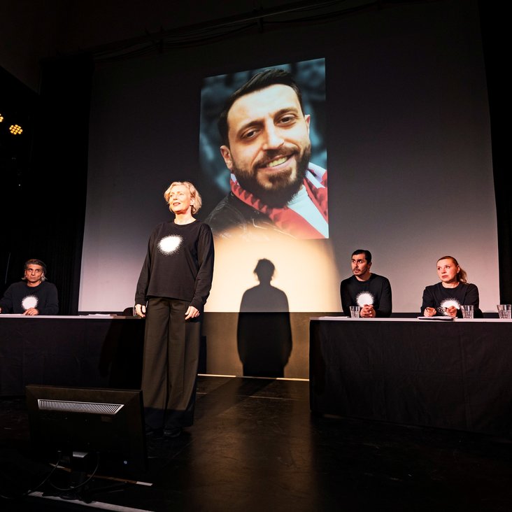 Die Schauspieler:innen von "And now Hanau" auf der Bühne. Sie tragen alle schwarze Kleidung mit einem vollflächig weißen Kreis auf der Brust.