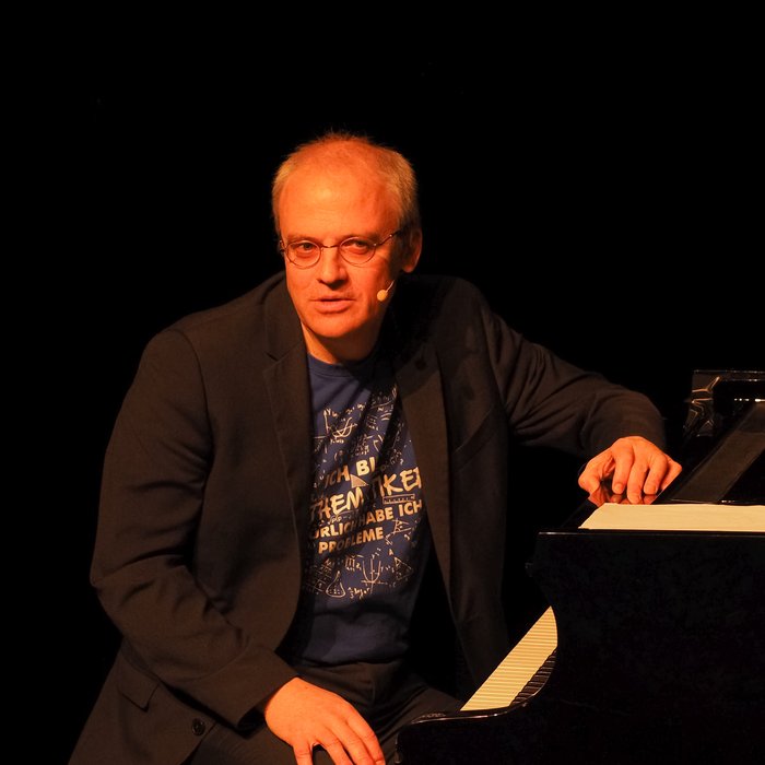 Kabarettist Tim Sigg sitzt am Klavier und schaut in die Kamera