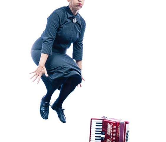 Carmela de Feo springt in die Luft, neben ihr steht ein rotes Akkordeon auf dem Boden