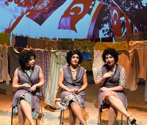 Drei Frauen sitzen vor Wäscheleinen auf Stühlen