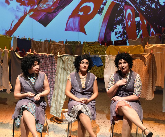 Drei Frauen sitzen vor Wäscheleinen auf Stühlen