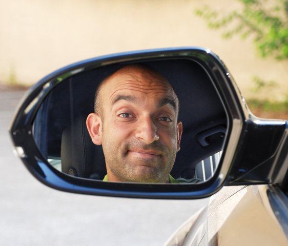 Django Asül lächelt. Man sieht sein Spiegelbild im Rückspiegel eines Autos.