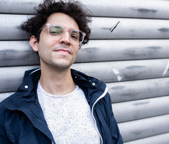 Porträt eines Mannes im Freien vor einer Metallwand, seitlicher Blick, natürliche Lichtstimmung.