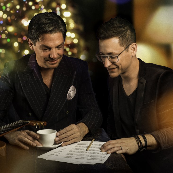 Die beiden Café del Mundo Musiker stehen am Flügel, darauf steht eine Kaffeetasse und es liegen Notenblätter und ein Stift daneben