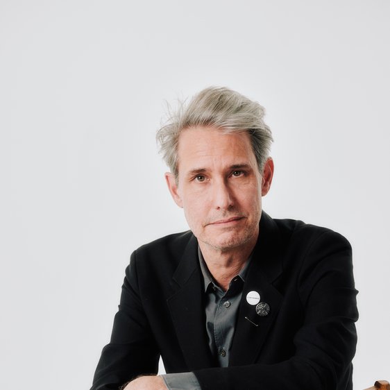 Dirk von Lowtzow sitzt seitlich auf einem Stuhl und blickt in die Kamera.