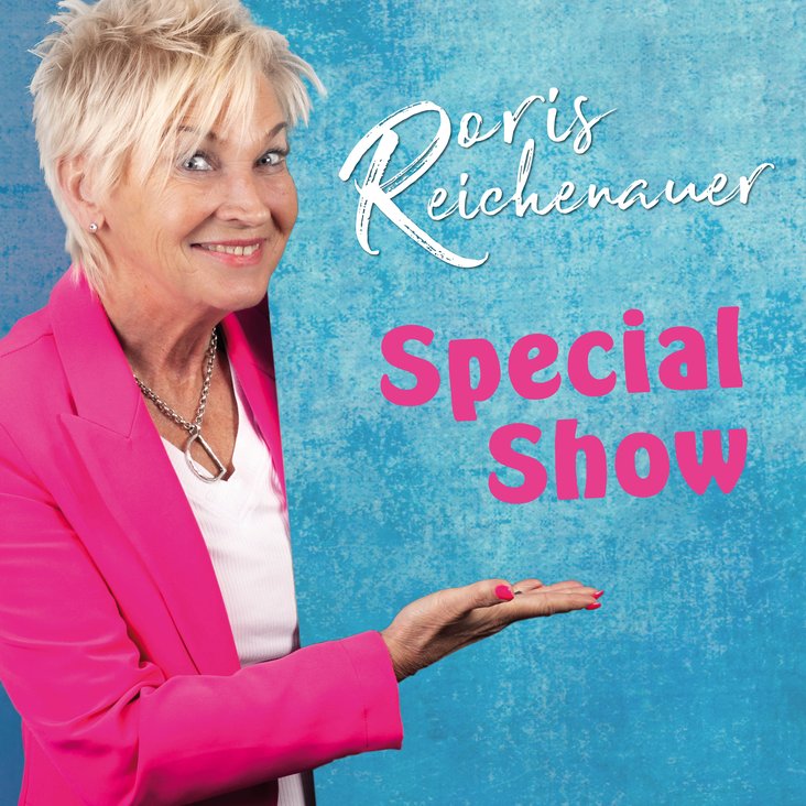 Die Künstlerin schaut grinsend in die Kamera und präsentiert dabei den Schriftzug der Show