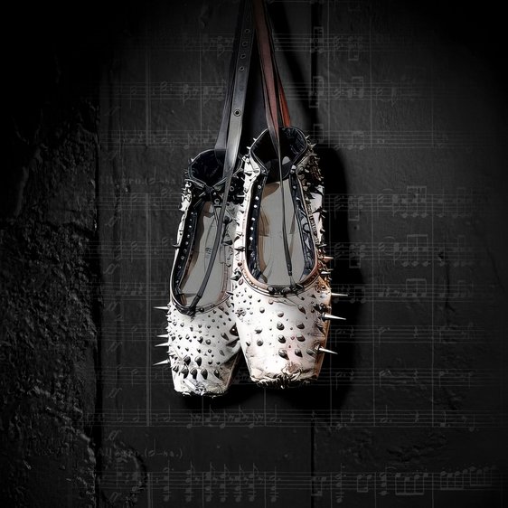 Ein Paar weißer Spitzenschuhe mit Nieten hängt vor einem schwarzen Hintergrund, der mit Musiknoten beschriftet ist.