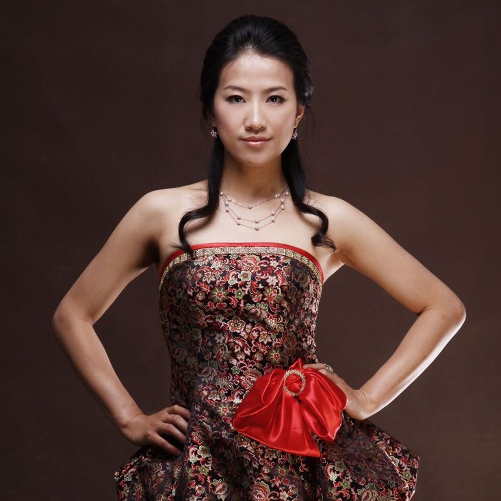 Eine junge, asiatisch gelesene Frau in einem Kleid posiert selbstbewusst