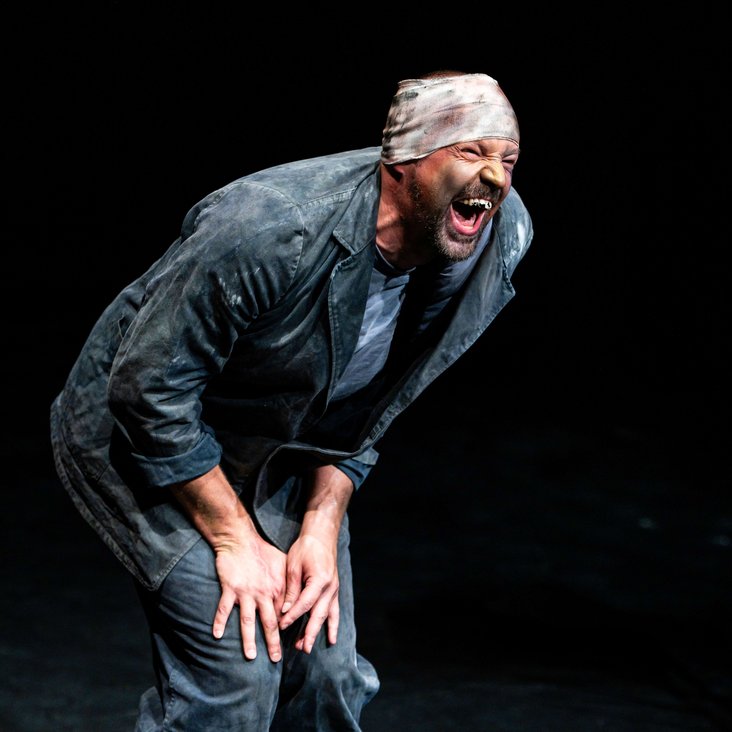 Der Künstler steht mit aufgerissenem Mund und verbundenem Kopf auf der Bühne.