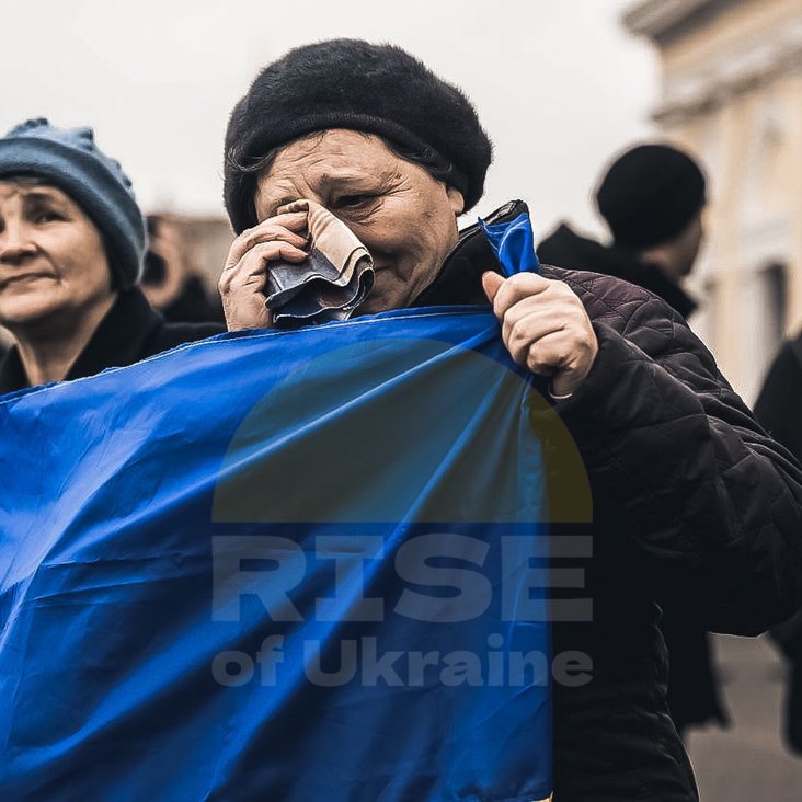 Eine weinende alte Frau wischt sich die Tränen mit einem Tuch weg. In der anderen Hand hält sie eine Ukraine-Flagge.