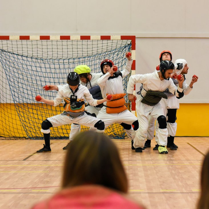 Teilnehmende der Performance in einer Sporthalle, einige davon tragen weiße Oberteile oder Anzüge.