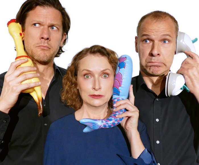 Die drei Protagonist:innen von Tauschrausch halten sich jeweils einen Telefonhörer, eine Gummihenne und einen aufblasbaren kleinen Wal als Telefon ans Ohr.