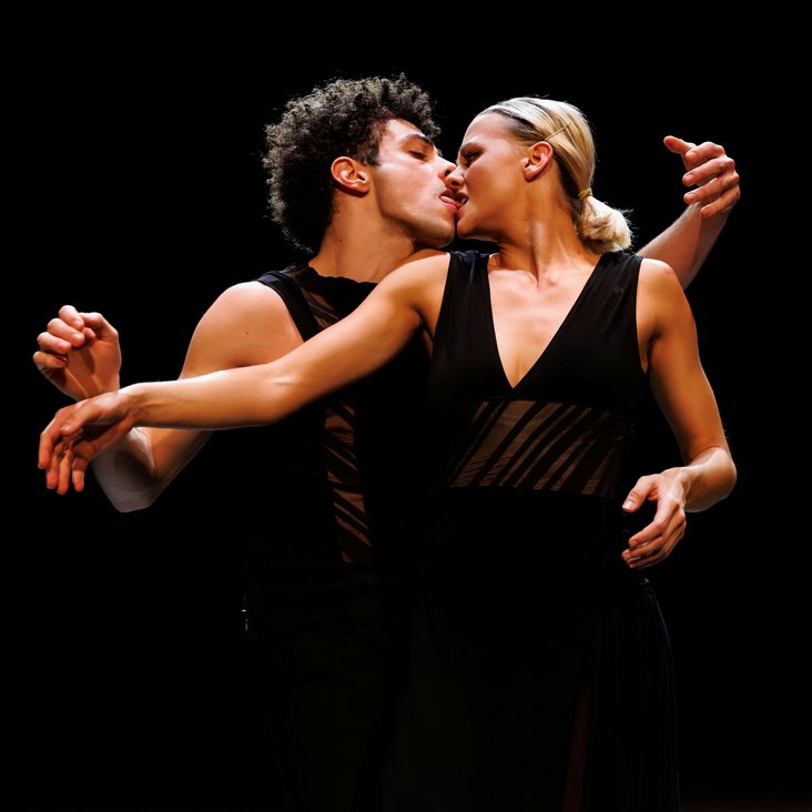 Tänzer:innen in Kostüm auf der Bühne, der Boden ist schwarz und die Bühne ist professionell ausgeleuchtet.