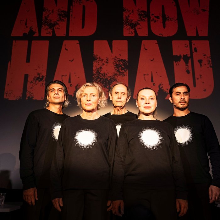 Die Schauspieler:innen von "And now Hanau" auf der Bühne. Sie tragen alle schwarze Kleidung mit einem vollflächig weißen Kreis auf der Brust.