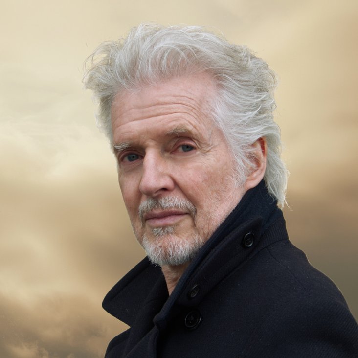 Das Portrait eines Mannes mit grauen Haaren. Er trägt eine schwarze Jacke.