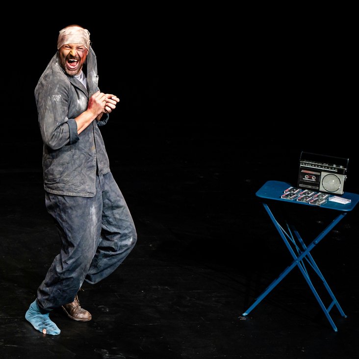 Der Künstler steht mit leicht gebeugten Beinen vor schwarzem Hintergrund auf der Bühne.