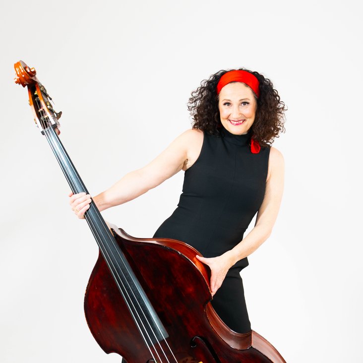 Anette Heiter mit schwarzem Kleid und rotem Haarband, sie hält einen Kontrabass vor sich stehend.