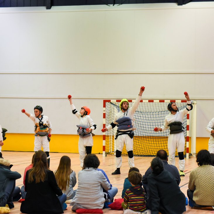 Teilnehmende der Performance in einer Sporthalle, einige davon tragen weiße Oberteile oder Anzüge.