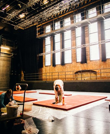 On the stage area of Hall T1, a stage set is painted by a staff member.