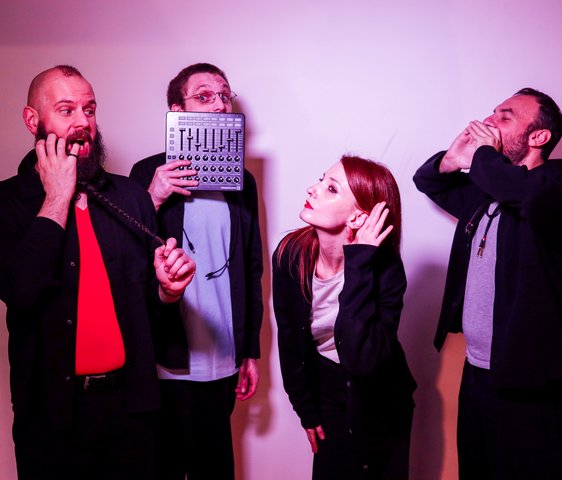 Vier Performer:innen improvisieren gestisch und stimmlich vor neutralem Hintergrund.