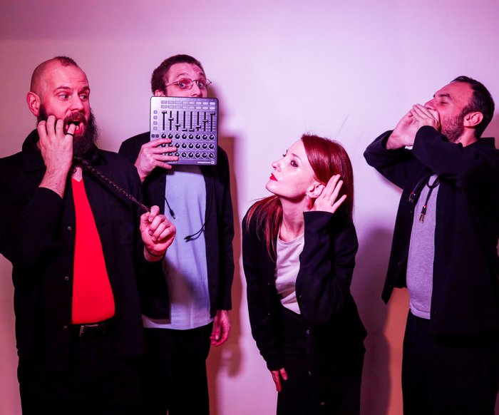 Vier Performer:innen improvisieren gestisch und stimmlich vor neutralem Hintergrund.