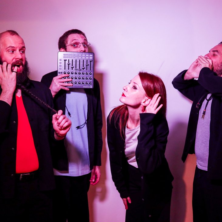 Vier Performer:innen improvisieren gestisch und stimmlich vor neutralem Hintergrund.