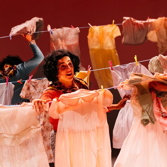 Drei Frauen hängen auf der Bühne bunte Kleidungsstücke auf eine Wäscheleine