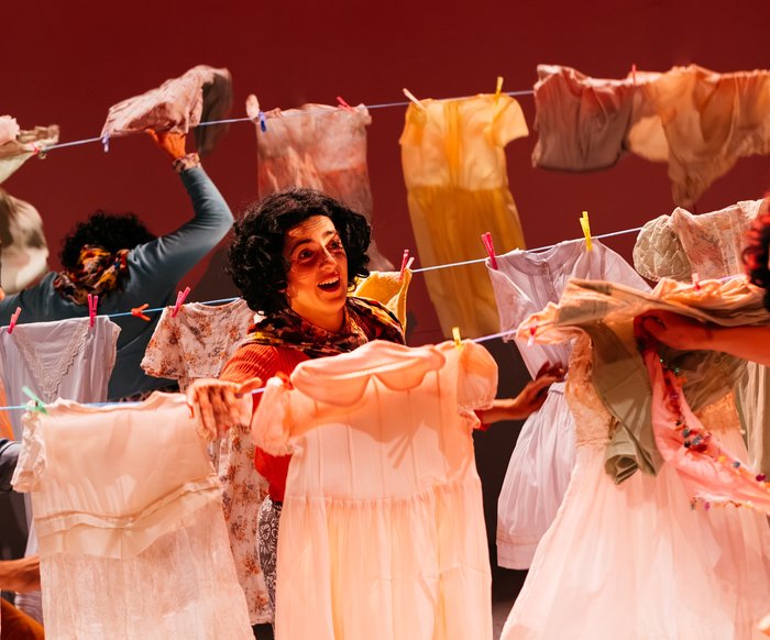 Drei Frauen hängen auf der Bühne bunte Kleidungsstücke auf eine Wäscheleine