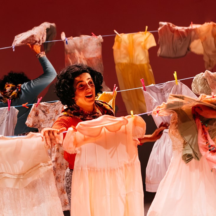 Drei Frauen hängen auf der Bühne bunte Kleidungsstücke auf eine Wäscheleine
