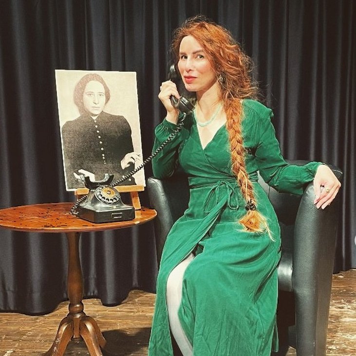 Eine Frau sitzt auf einem Sessel und hat ein altes Schnurtelefon am Ohr.