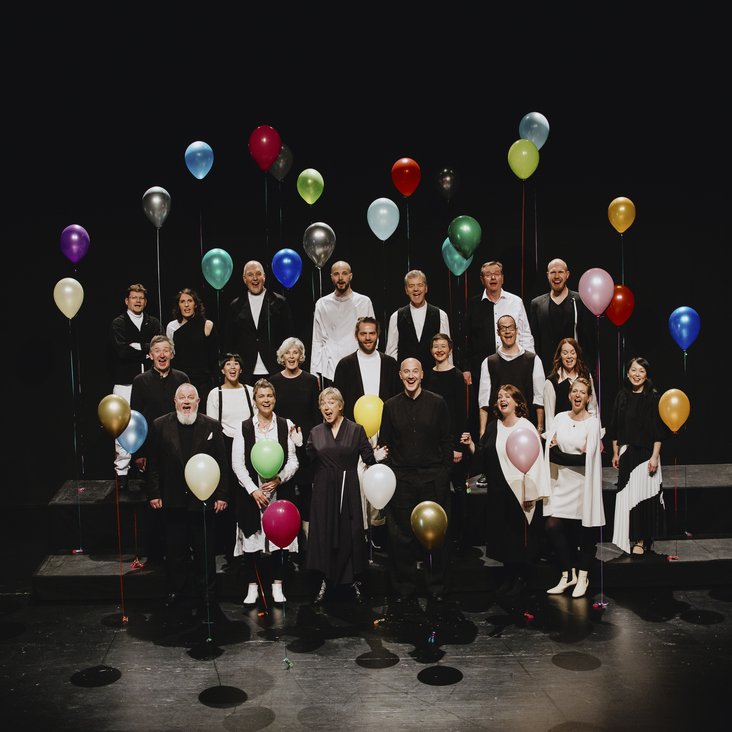 Das SWR Vokalensemble auf der Bühne, alle Beteiligten haben einen Luftballon an einer Schnur in der Hand